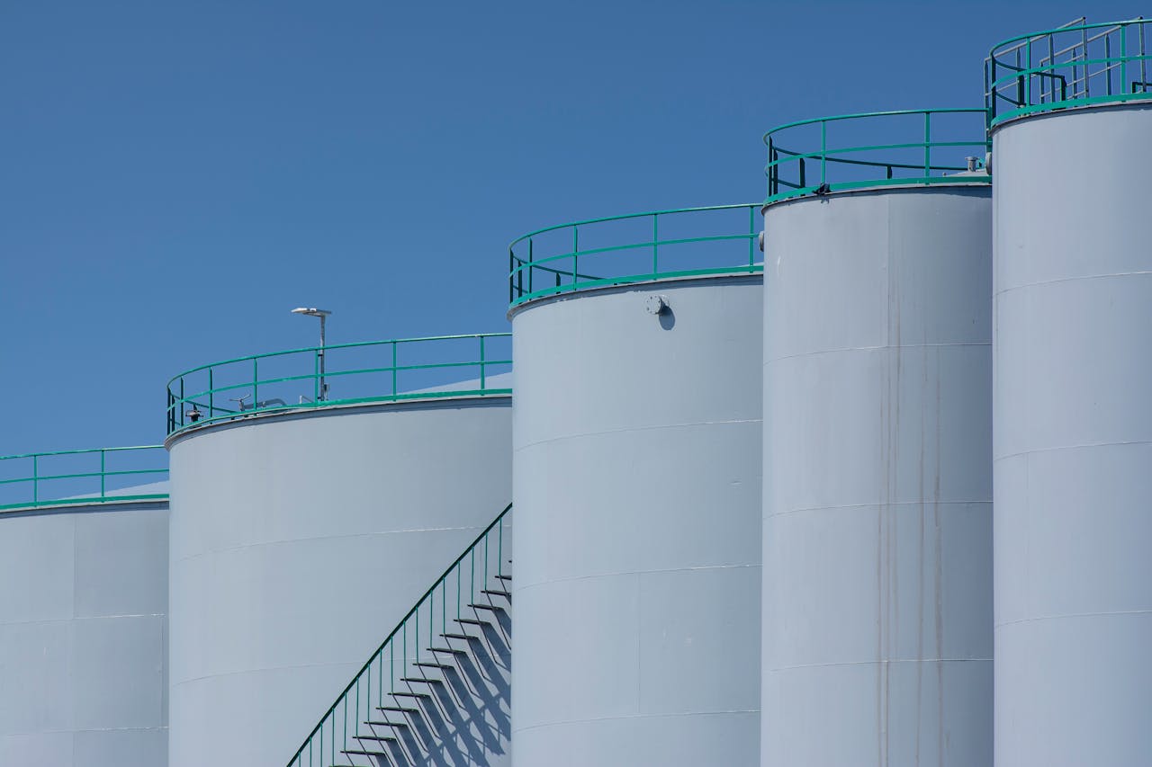 about-us Large industrial storage tanks with green railings against a clear blue sky.